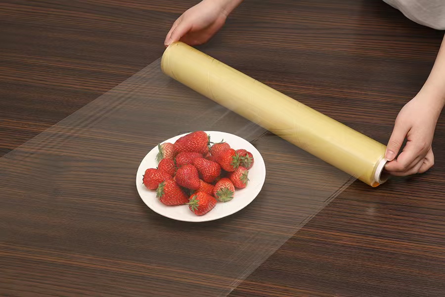 Hand wrapping a strawberry plate with transparent PVC film